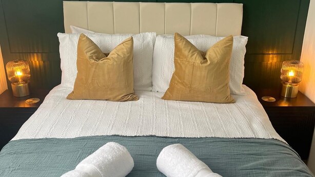 A neatly made bed with a headboard, two pillows, and two rolled towels on a green bedspread. - Modern Classic 2 Bed Apartment Near Graves Park (Sheffield)