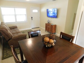 A dining area with a wooden table, chairs, a television mounted on the wall, and a door in the background. - Peaceful 3-bedroom house in San Mateo, FL (San Mateo)