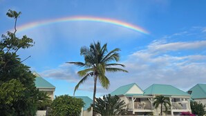 A residential area with houses, palm trees, and a rainbow. - Incredible sea view apartment 🌊 - Swimming pool - Terrace - (Saint-Martin)