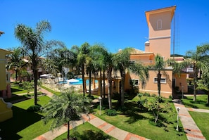 A resort with a pool, palm trees, and a building with a tower. - Casa Elegante a 100 metros do Mar (Governador Celso Ramos)