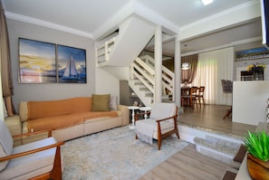 A living room with a sofa, armchairs, a coffee table, a staircase, and a dining area. - Casa Elegante a 100 metros do Mar (Governador Celso Ramos)
