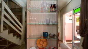Un escalier menant à un palier où se trouve une étagère en verre, sur laquelle sont exposés divers objets en verre et de la vaisselle.
