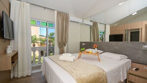 Une chambre d’hôtel comprenant un lit, une table de chevet, une télévision, un balcon avec des rideaux et un grand miroir.