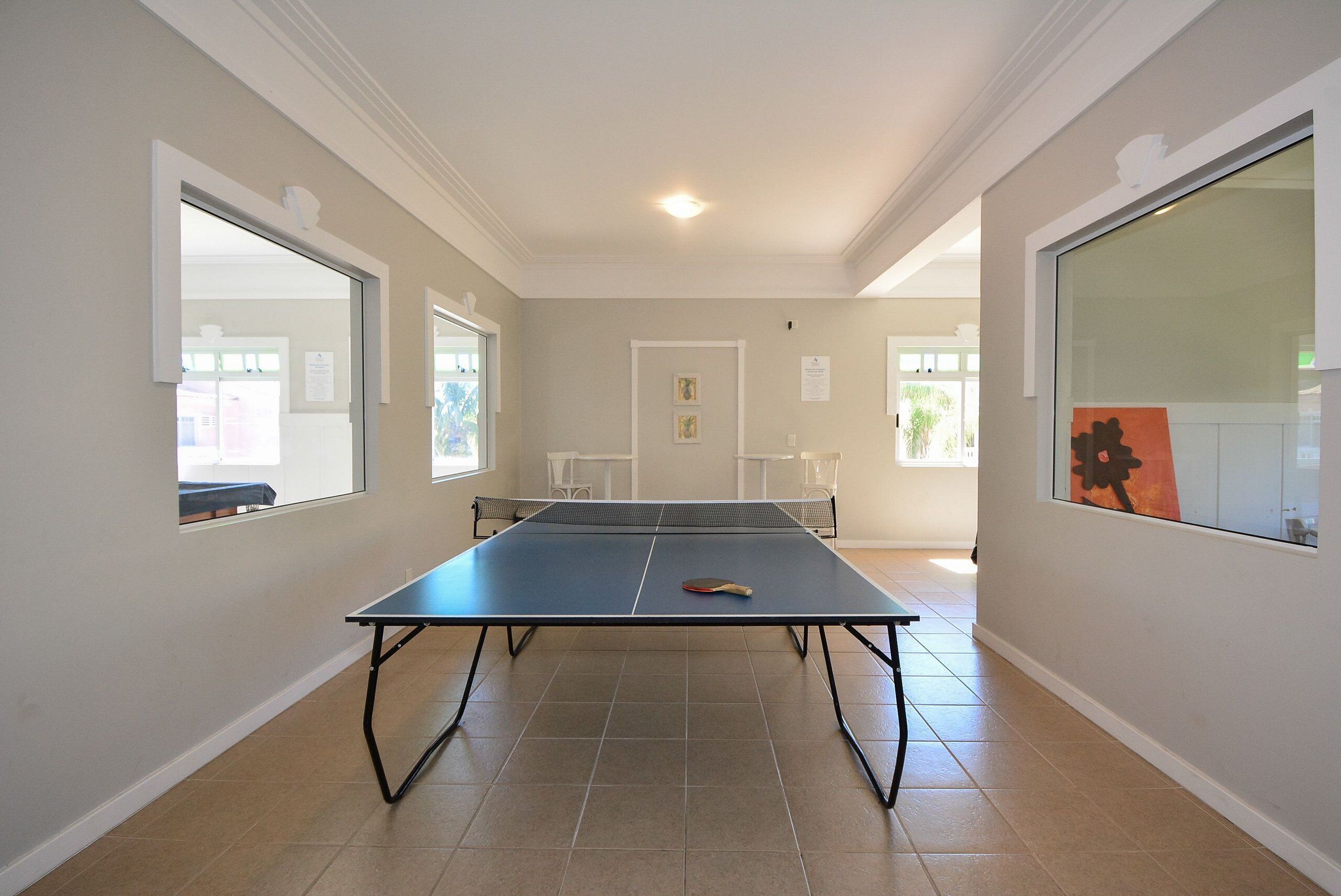 Una habitación con mesa de ping pong, paredes blancas y una puerta que da a otra estancia.