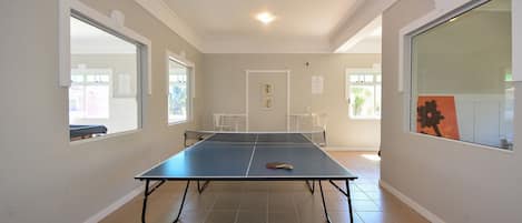 Una habitación con mesa de ping pong, paredes blancas y una puerta que da a otra estancia.