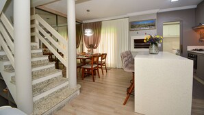 Une cuisine moderne dotée d’un îlot central, d’un coin repas avec des chaises en bois et d’un escalier avec une rampe en verre.