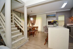 Eine moderne Küche mit einer zentralen Kochinsel, einem Essbereich mit Holzsesseln und einer Treppe mit Glastrennwand.