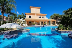 A hotel with a swimming pool, palm trees, and a tiled deck. - Casa Elegante a 100 metros do Mar (Governador Celso Ramos)