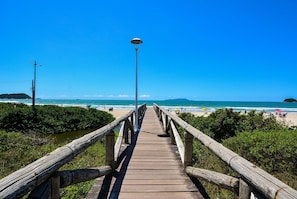 A wooden boardwalk leading to a beach with a clear blue sky. - Casa Elegante a 100 metros do Mar (Governador Celso Ramos)