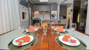 Un coin repas avec une table en bois dressée pour quatre personnes, un vase de fleurs et une cuisine en arrière-plan.