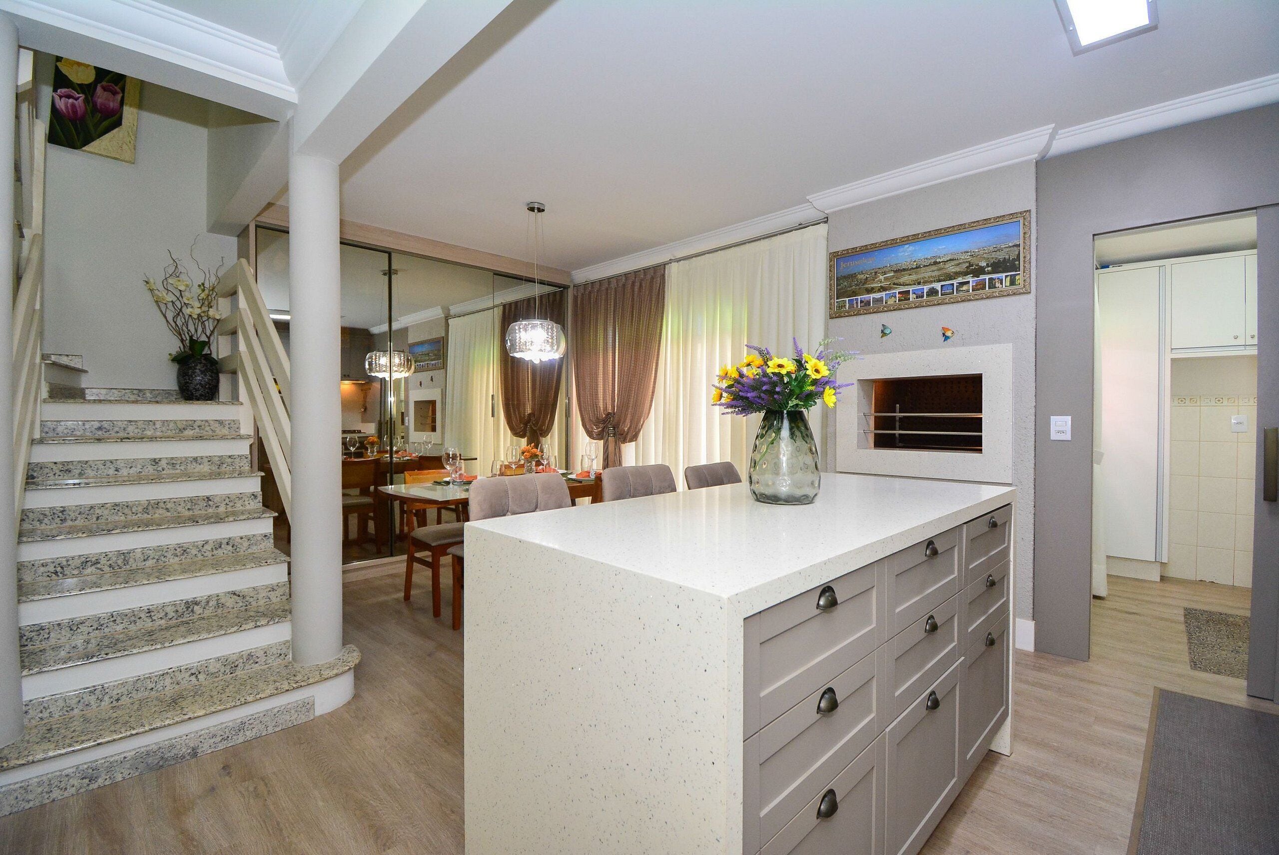 A modern kitchen with a central island, a dining area with a chandelier, and a staircase leading to another level.