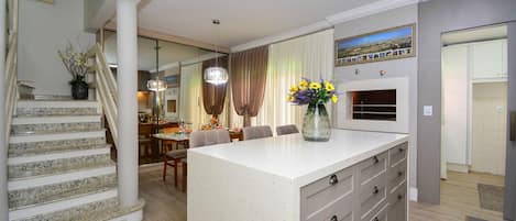 A modern kitchen with a central island, a dining area with a chandelier, and a staircase leading to another level.