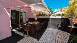 Une terrasse avec une table et des chaises, un espace abrité et un bâtiment à la façade rose.