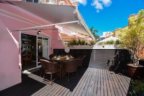 Eine Terrasse mit Tisch und Stühlen, ein überdachter Bereich und ein Gebäude mit rosa Fassade.