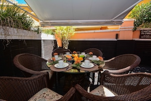 Un área de comedor al aire libre con sillas de mimbre y una mesa redonda para cuatro personas, rodeada por un toldo blanco.