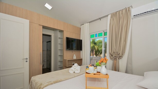 Une chambre d’hôtel avec un lit, un téléviseur fixé au mur, une armoire en bois et une fenêtre avec des rideaux.