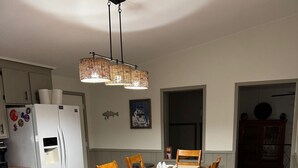 En matplats med ett träbord, stolar, en vit matta, en hängande lampa och ett kylskåp.