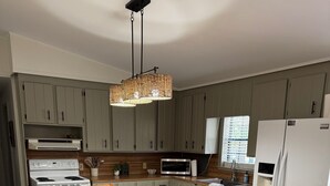 En matplats med ett träbord, stolar, en flätad lampa och ett kök i bakgrunden.