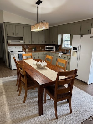 A dining area with a wooden table, chairs, a woven light fixture, and a kitchen in the background. - Cozy 2-bedroom renovated mobile home in serene Steinhatchee with Back Patio (Steinhatchee)