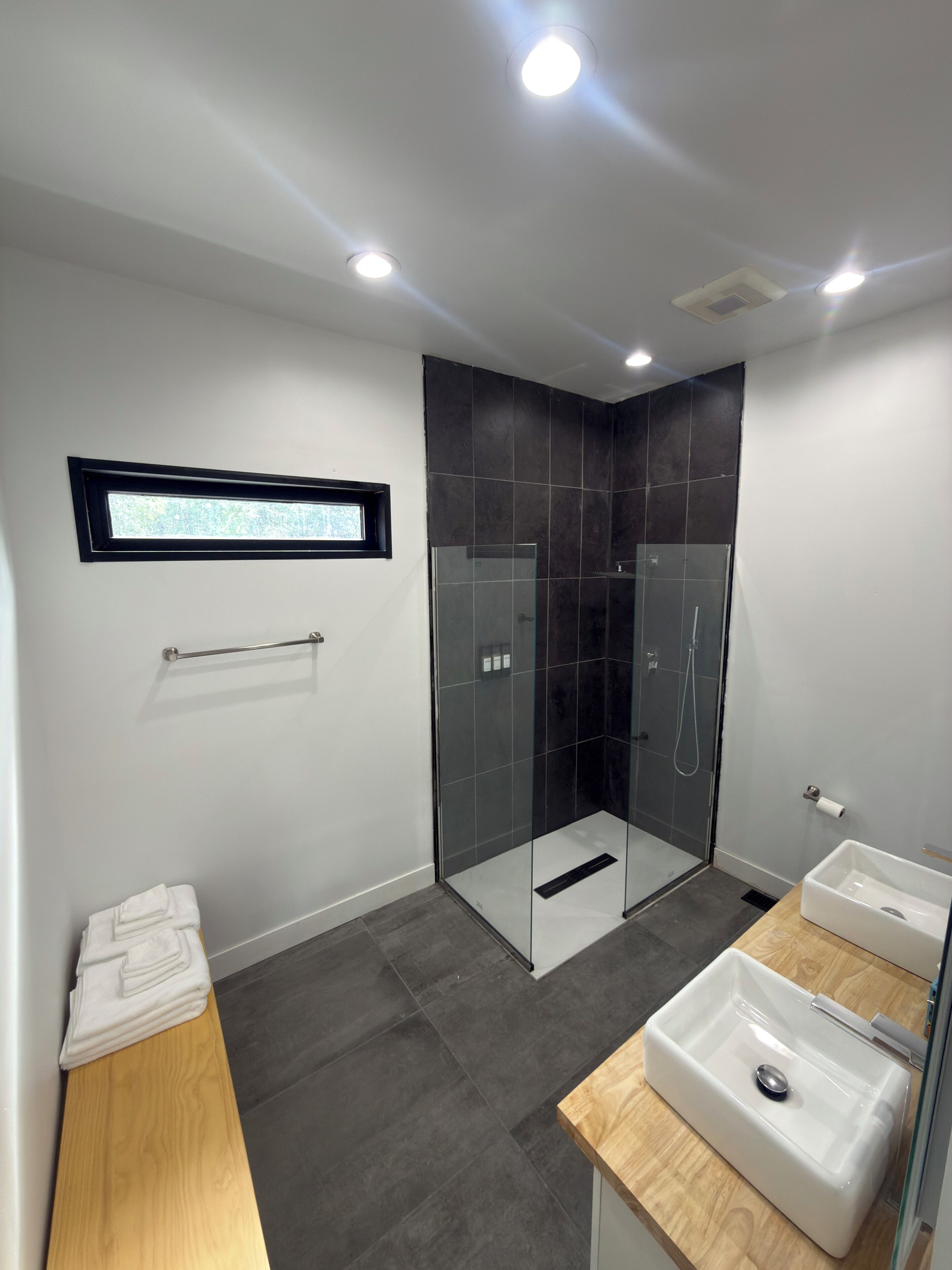 Ein modernes Badezimmer mit einer gläsernen Duschkabine, einem Holzwaschtisch und einem weißen Waschbecken.