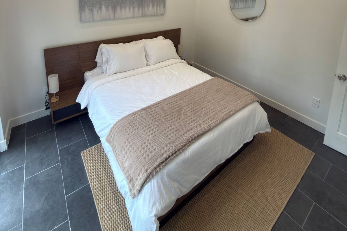 Ein Schlafzimmer mit einem Bett, einer Wand-Klimaanlage, einem Gemälde und einem runden Spiegel.