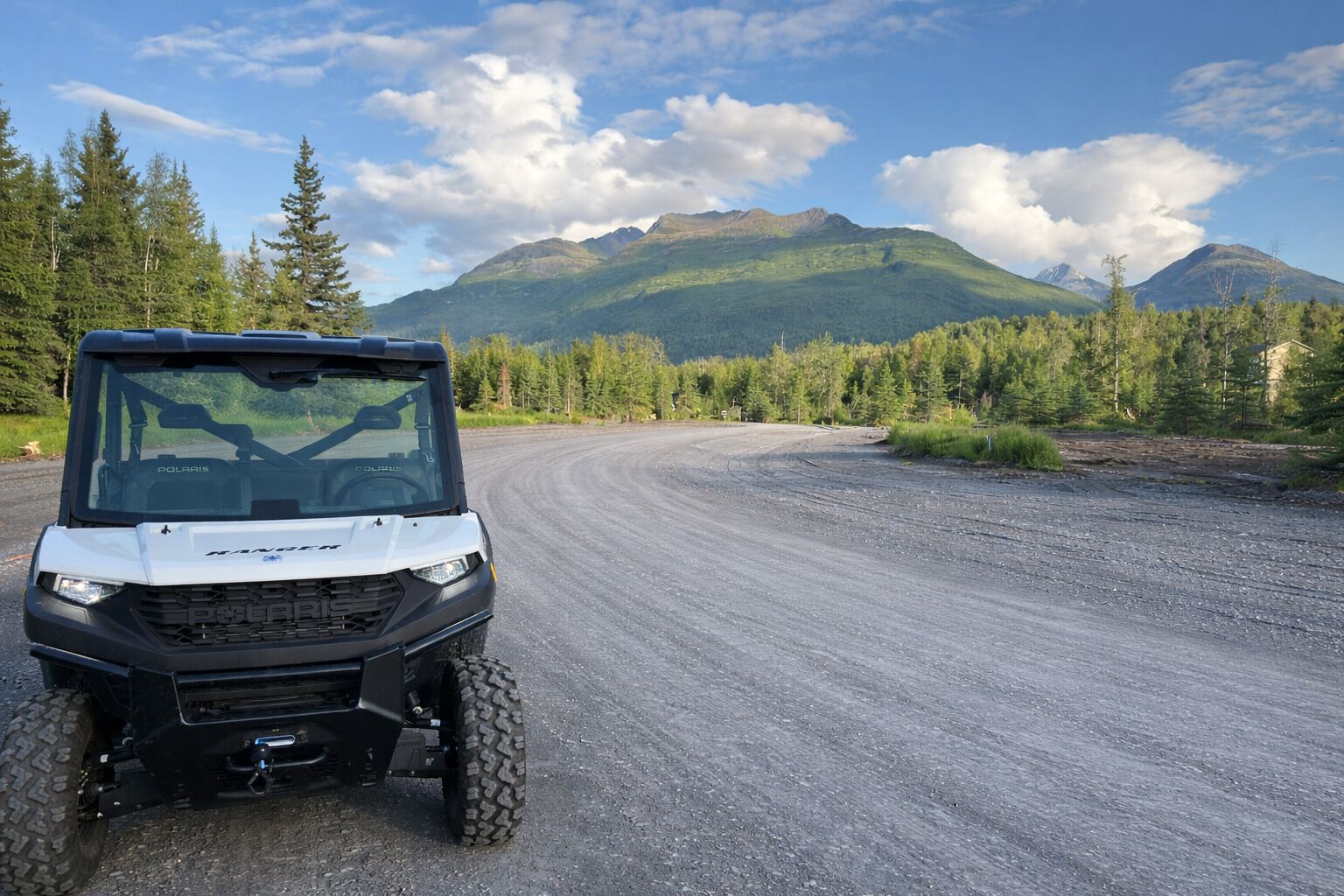 Un vehículo Polaris Ranger en un camino de grava con montañas al fondo.