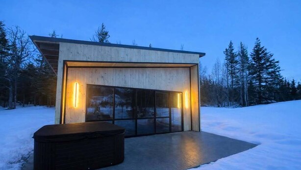 A modern building with large glass windows and a wooden exterior, surrounded by snow and trees.
