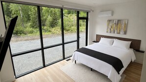 A modern bedroom with a large bed, a view of greenery outside, and a minimalist design.