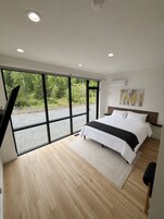 A modern bedroom with a large bed, a view of greenery outside, and a minimalist design.