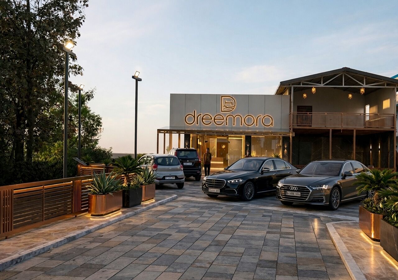 Un edificio moderno con un llamativo letrero 'dreamora', que cuenta con una entrada espaciosa, un área exterior techada y varios coches estacionados.