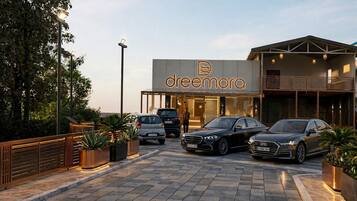 A modern building with a prominent 'dreamora' sign, featuring a spacious entrance, a covered outdoor area, and several parked cars.