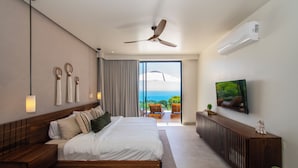 Une chambre moderne équipée d’un lit, d’un ventilateur de plafond, d’un climatiseur, d’une télévision et offrant une vue sur l’océan.
