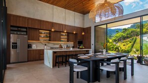 Une cuisine moderne dotée d’un îlot central, de meubles en bois, de luminaires suspendus et d’un grand espace de salle à manger avec des chaises.