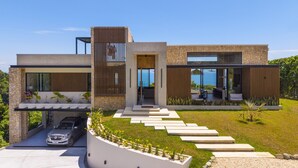 Une maison moderne avec une façade en pierre, de grandes fenêtres et une allée menant à une voiture garée.