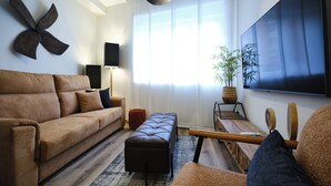Un salon moderne comprenant un canapé, un pouf, une table basse et un grand téléviseur à écran plat fixé au mur.