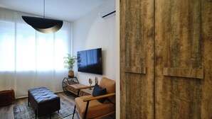 Un salon moderne avec un canapé, un pouf et un téléviseur fixé au mur.