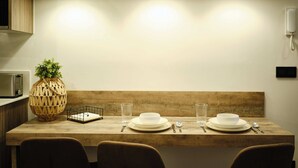 Une table à manger dressée avec des assiettes, des verres et des couverts, éclairée par trois lampes suspendues, avec un téléphone fixé au mur et un vase décoratif posé sur la table.