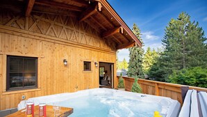 Une cabane en bois avec un jacuzzi, une terrasse en bois et une vue sur les arbres.