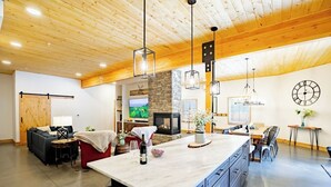 Un vaste espace de vie doté d’un grand plafond en bois, d’une cheminée en pierre, d’une table à manger avec des chaises et d’un îlot de cuisine.