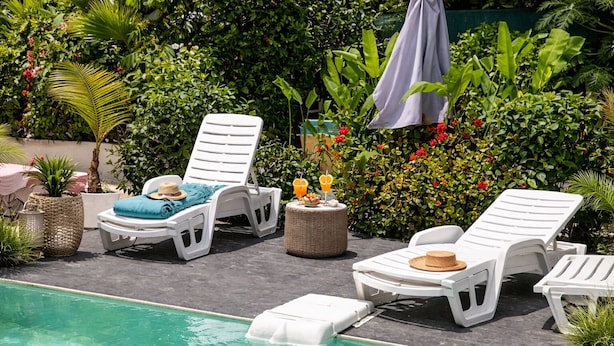 Un espace aménagé au bord de la piscine, avec des chaises longues, une petite table et une plante en pot.