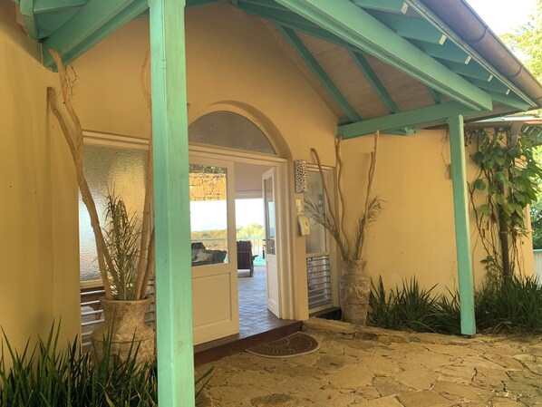 A covered porch with stone flooring, a door leading inside, and potted plants.