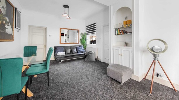 Ein modernes Wohnzimmer mit einer Couch, Sesseln, einem Couchtisch, einer Stehlampe und einem Bücherregal.