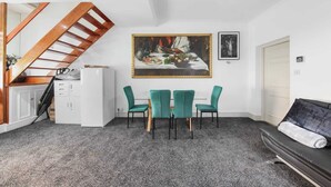 Ein Essbereich mit Tisch und Stühlen, einem Gemälde über dem Tisch, einer Treppe und einem Sofa.