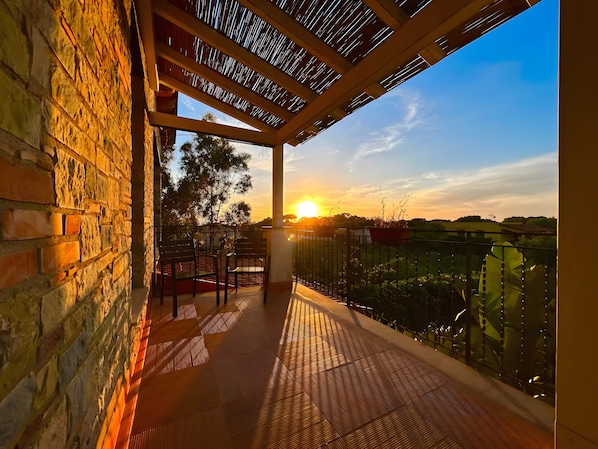 Ein Balkon mit Blick auf den Sonnenuntergang, eine Backsteinmauer und ein Metallgeländer.
