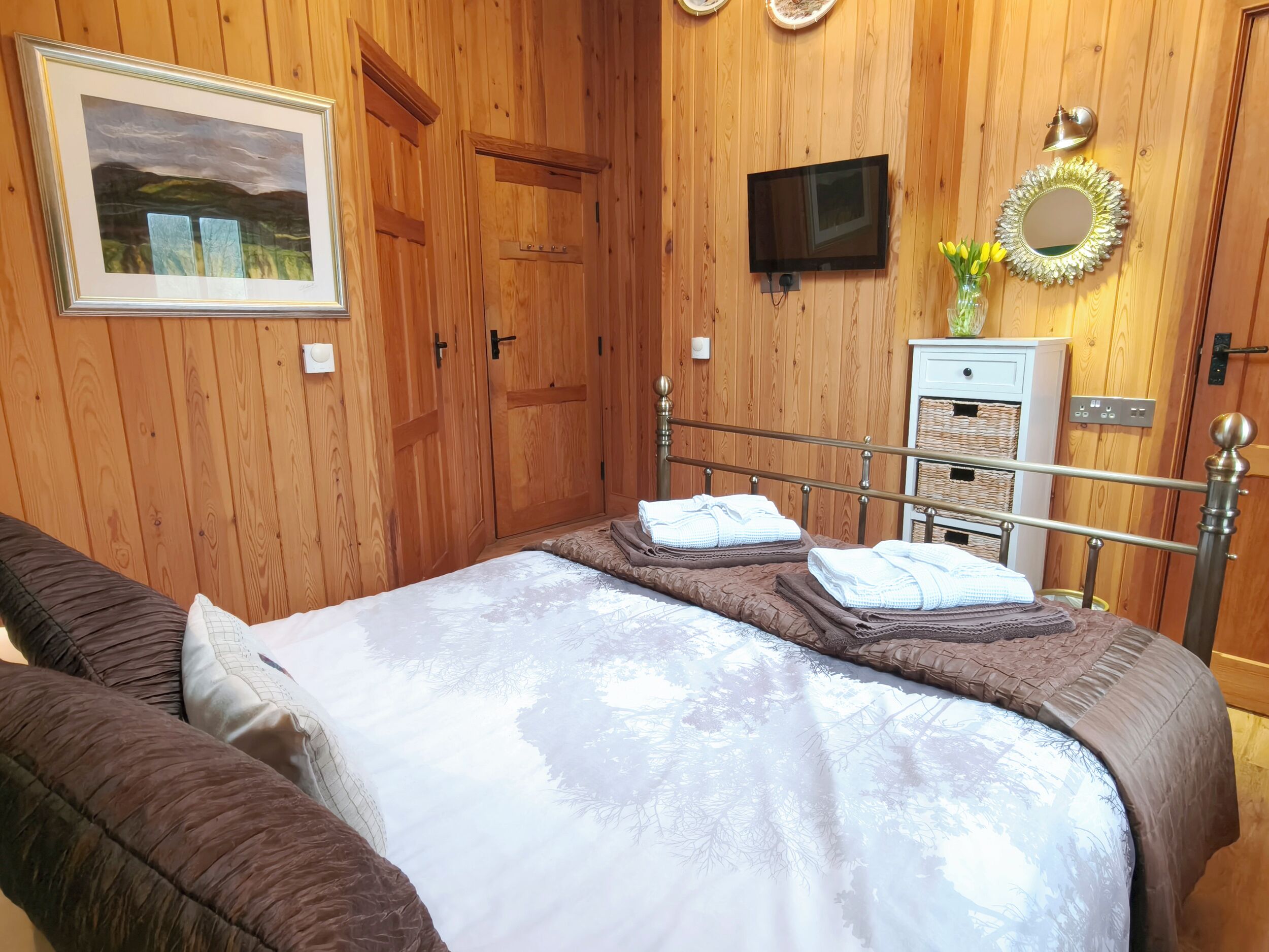 Un dormitorio con cama, televisor, espejo y paredes de madera.