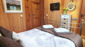 Un dormitorio con cama, televisor, espejo y paredes de madera.