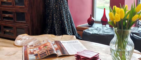 A wooden table with a magazine, a stack of red cards, and a vase with yellow flowers.