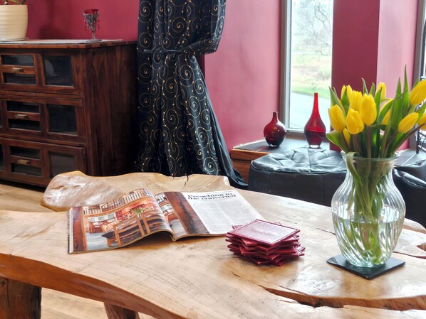 Una mesa de madera con una revista, una pila de cartas rojas y un florero con flores amarillas.