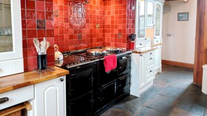 A kitchen with red tiles, a black stove, and white cabinets. - Kaber Chapel (Kirkby Stephen)