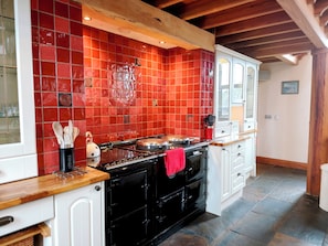 A kitchen with red tiles, a black stove, and white cabinets. - Kaber Chapel (Kirkby Stephen)